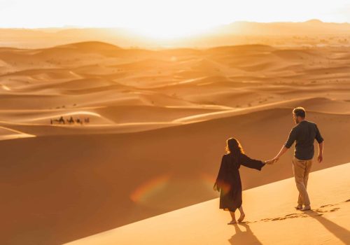 Couple walking in Sahara desert at sunset. View from behind, nature background. Travel, freedom and wanderlust concept.